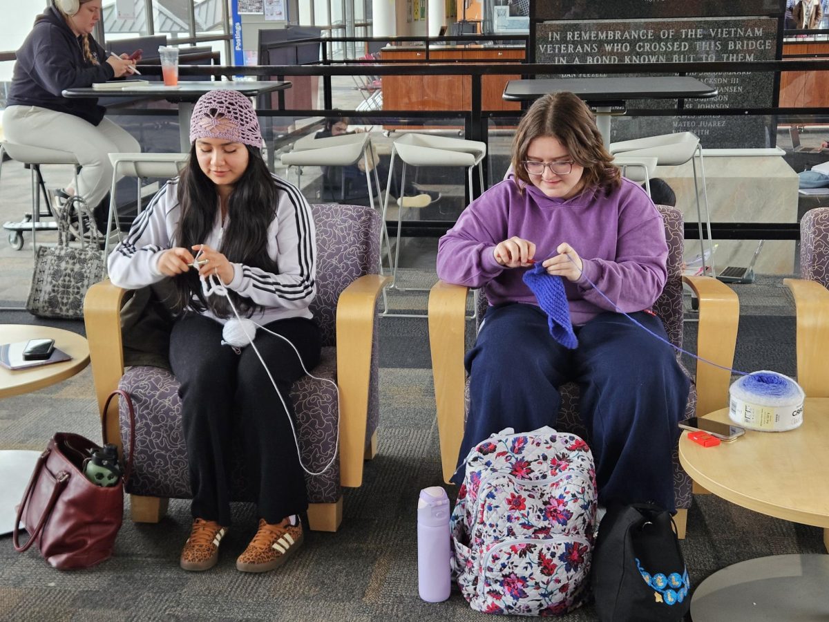 Joliet Junior College students Alisia Hernandez and Shelby Doss sitting side by side smiling as they work on their own crocheting projects during one of the weekly meetings for Stitch & Chat. 