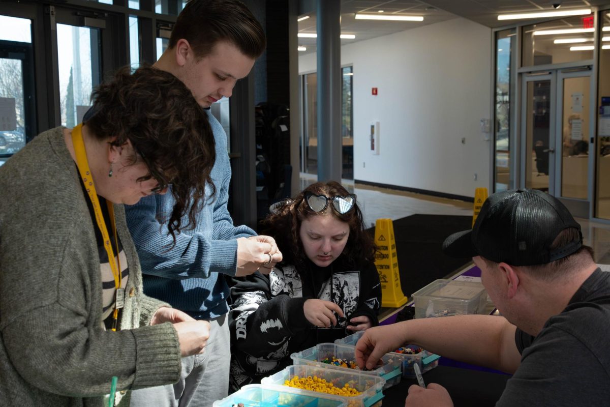 Worker from Bricks & Minifigs helping Staff member Connor Herrington, Andrea (Dre) Spreitzer, and student Harley Stockhausen build a Minifig at the "Build your own Lego Minifigure" event at the Romeoville Campus on March 18, 2026.