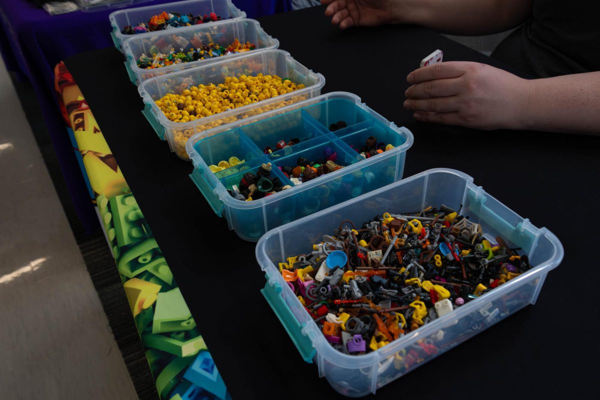 Bins with different parts to build your Minifig at the "Build your own Lego Minifigure" event at the Romeoville Campus on March 18, 2026. Bins contain pants/lower body, tops/upper body, face, and then accessories (left to right). 